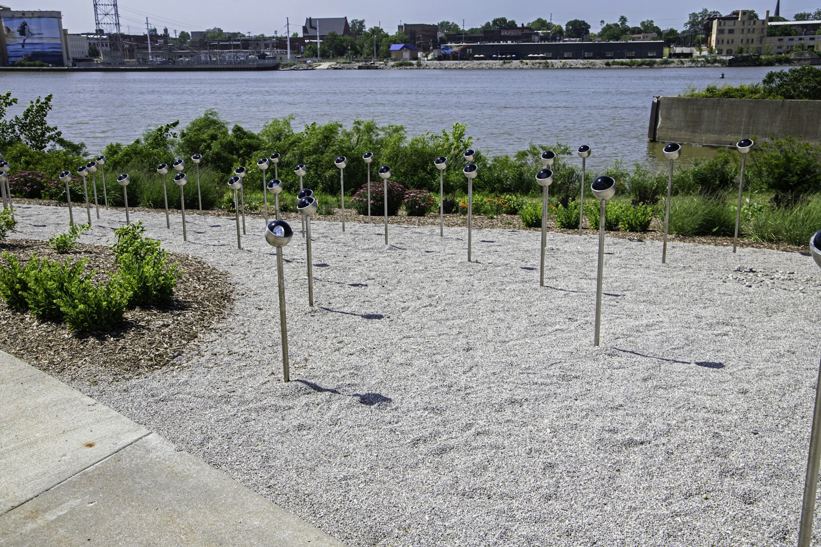Public art installation of metal poles in a riverside gravel garden at Glass City Metropark
