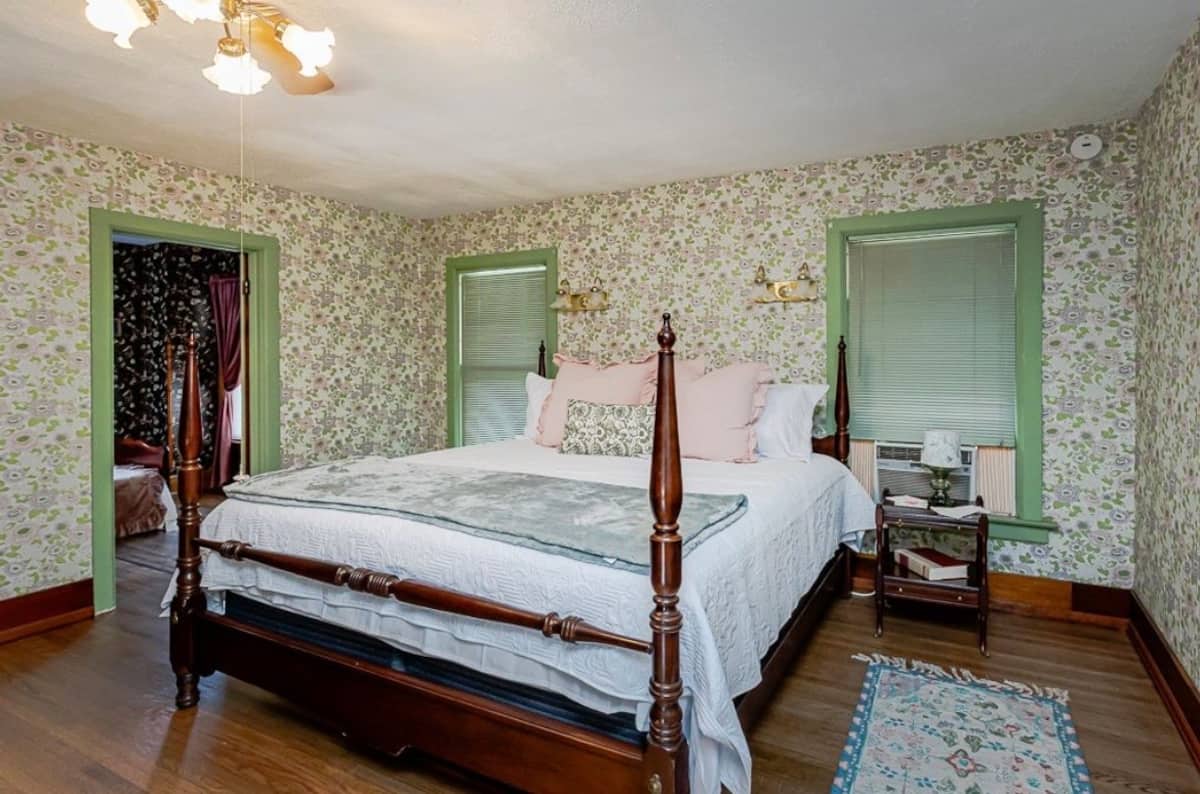 Bright bedroom with a dark wood four-poster bed, green trim and floral wallpaper