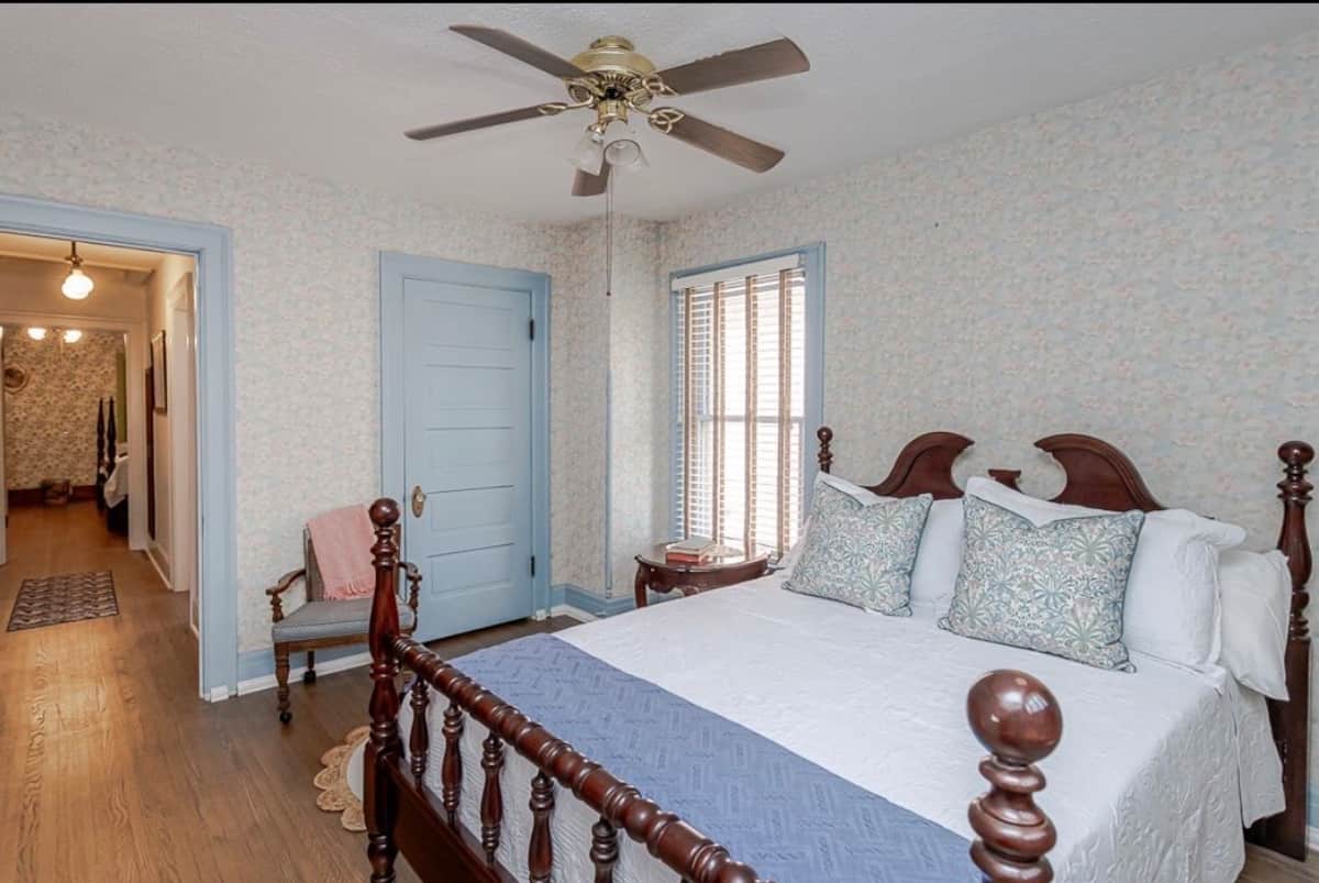 Light-filled bedroom with blue trim, a carved wood bed and soft patterned walls